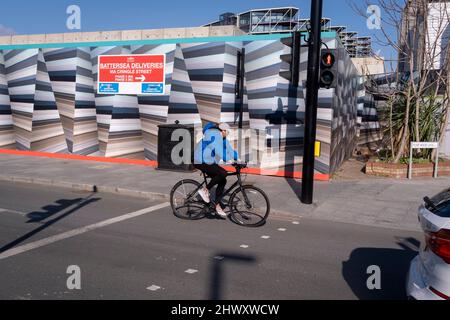 Un ciclista passa attraverso un edificio urbano e paesaggio di alberi su Pump House Lane a Nine Elms, il 7th marzo 2022, a Londra, Inghilterra. Foto Stock