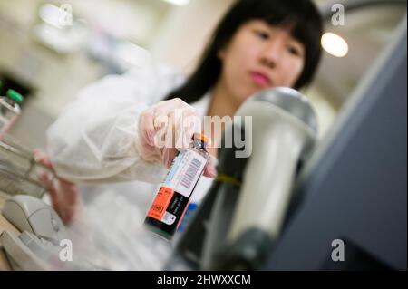 Un tecnico di laboratorio che esegue la scansione di un campione di sangue in una macchina di analisi Foto Stock