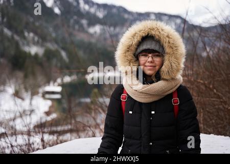 Giovane donna turistica in cappotto invernale con montagne sullo sfondo Foto Stock