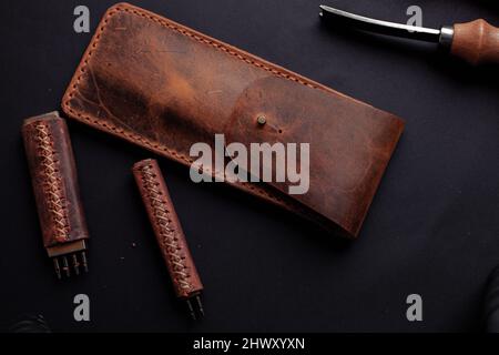 Custodia a matita in pelle fatta a mano. Strumenti Leathercraft con sfondo nero. Foto Stock