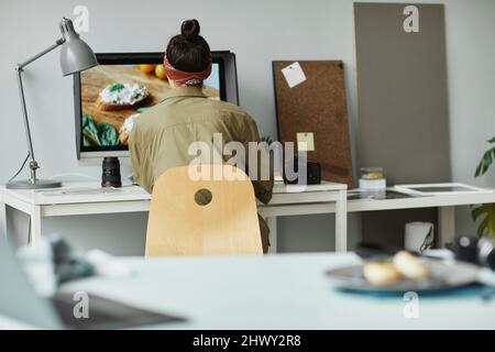 Vista posteriore del fotografo alimentare femminile utilizzando il computer mentre ritoccare le foto in studio, spazio copia Foto Stock