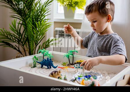 Bambino ragazzo concentrato con fiducia giocando in prima fase di sviluppo gioco cinetico sabbia Montessori materiale in casa accogliente. Adorabile bambino maschile gioca con carnivoro Foto Stock