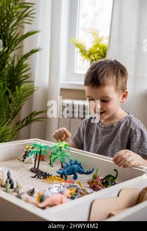 Bambino ragazzo concentrato con fiducia giocando in prima fase di sviluppo gioco cinetico sabbia Montessori materiale in casa accogliente. Adorabile bambino maschile gioca con carnivoro Foto Stock