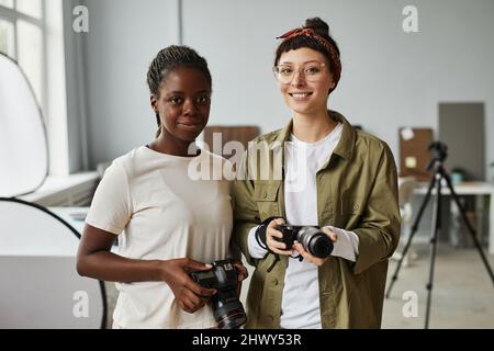 Vita in alto ritratto di due fotografi femmina sorridendo alla fotocamera mentre in piedi in studio fotografico, spazio copia Foto Stock