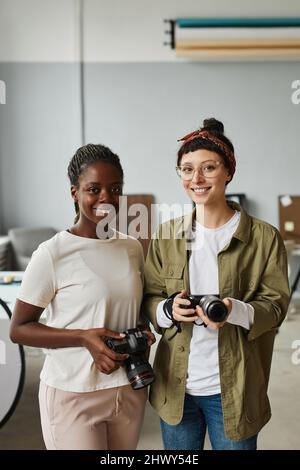 Ritratto verticale di due fotografi femmine che sorridono alla fotocamera mentre si trovano in studio fotografico Foto Stock