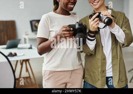 Scatto ritagliato di due fotografi sorridenti che tengono le fotocamere mentre lavorano in studio fotografico, spazio copia Foto Stock
