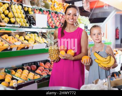 Giovane donna sorridente con figlia che prende vari frutti Foto Stock