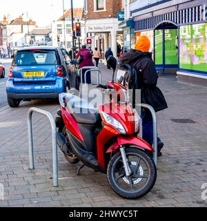 Epsom Surrey London UK, marzo 8 2022, Man Standing accanto A un Red Motor Scooter parcheggiato su un marciapiede Foto Stock