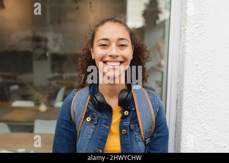 Ritratto di sorridente giovane afroamericana con cuffie wireless in città Foto Stock