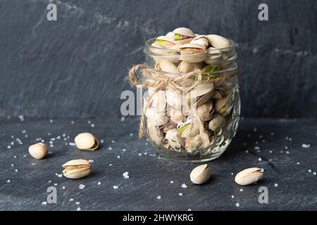 Pistacchi in un vaso di vetro con sale naturalmente su sfondo scuro Foto Stock