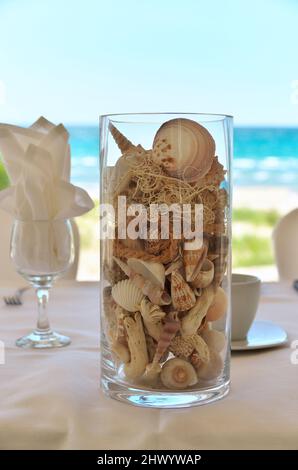 Un pezzo centrale di vetro Vase riempito con una varietà di conchiglie di mare per una festa nuziale sulla spiaggia Foto Stock