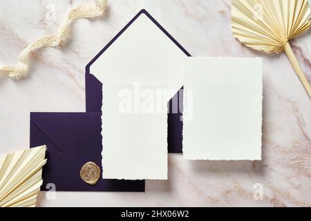 Elegante cancelleria per matrimoni. Carte di invito per matrimoni, buste viola, nastro di seta, fiori secchi su scrivania in pietra. Foto Stock
