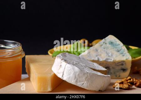 Tre formaggi - Camembert brie, blu camembert e parmigiano accatastati l'uno sull'altro accanto al miele, olive su un piatto e basilico Foto Stock