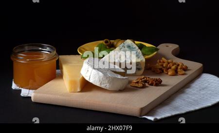 Tre formaggi - Camembert brie, blu camembert e parmigiano accatastati l'uno sull'altro accanto al miele, olive su un piatto e basilico Foto Stock