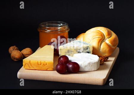 tre tipi di formaggio, miele, ciambelle, uva e noci su sfondo nero Foto Stock