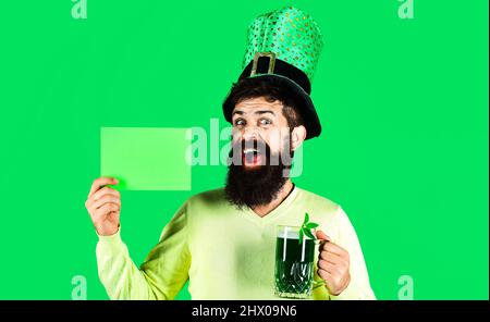 Giorno delle Patricks. Felice uomo Bearded in cappello con birra verde tiene bordo con spazio di copia per la pubblicità. Foto Stock