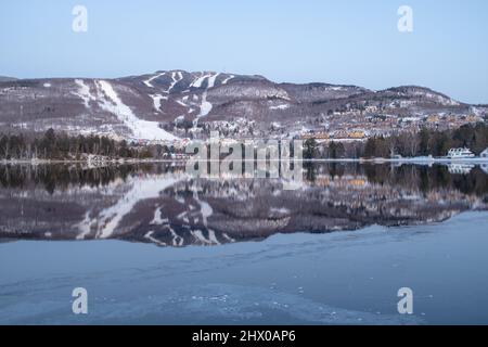 Le piste da sci di Mont-Tremblant si riflettono in un lago, in una giornata invernale parzialmente soleggiata e nebulosa Foto Stock
