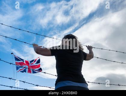 Vista posteriore della donna al controllo della recinzione di confine con bandiera britannica. Immigrazione britannica, politica dei visti, Ucraina, Russia conflitto rifugiati, Brexit, Confine UE... concetto Foto Stock