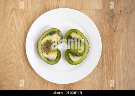 Immagine piatta di due metà di un kiwi a forma di cuore su un piatto bianco su una superficie di legno Foto Stock