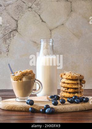 Caffè Dalgona in un bicchiere trasparente con biscotti al mirtillo e mirtilli su un asse di legno. Sfondo rustico parete. Caffè coreano molto alla moda. Foto Stock