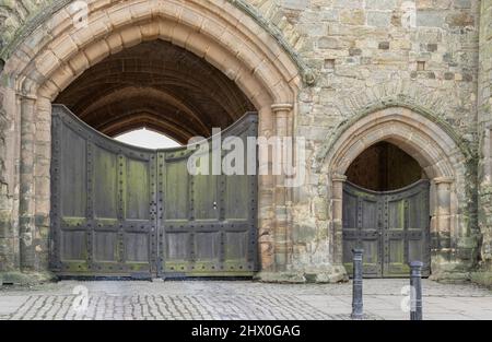 Una grande e piccola porta ad arco di pietra color miele in un castello con un cancello nero su ogni arco con borchie Foto Stock