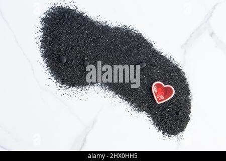 Cuore su sabbia nera con sfondo di marmo bianco. Foto Stock
