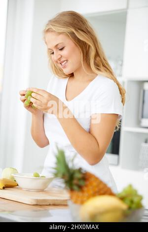 Queste uve sono così dolci. Giovane donna curvacea che mangia uva in cucina. Foto Stock