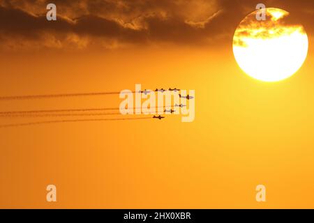 Formazione di velivoli viaggiando oltre un grande sole luminoso Foto Stock