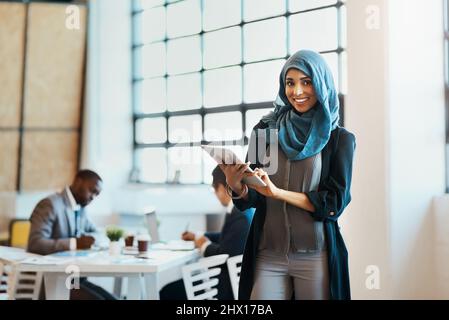 Tiene traccia dell'avanzamento del lavoro nell'azienda. Ritratto di una giovane e sicura donna d'affari che naviga su un tablet digitale mentre si trova in piedi nella Foto Stock