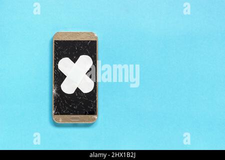 Broken Mobile Smart Phone con schermo incrinato è cerotto medico cerotto coperto di aiuto di banda su sfondo blu Flat Lay, concetto Foto Stock