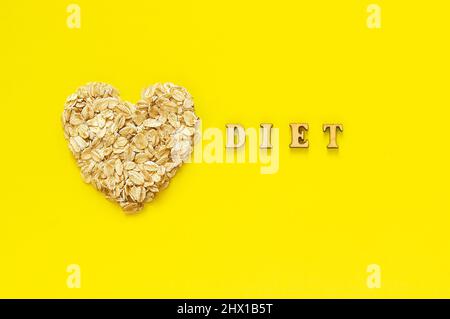 Texte sur Diet e fiocchi d'avena in forma di cuore su sfondo giallo. Concetto di dieta organica Helthy. Vista dall'alto Foto Stock