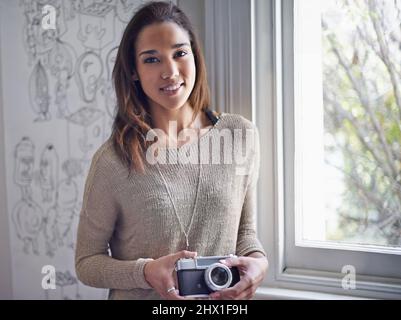 È ciò che ho sempre sognato di fare. Una giovane fotografa in piedi vicino a una finestra mentre tiene la sua macchina fotografica. Foto Stock