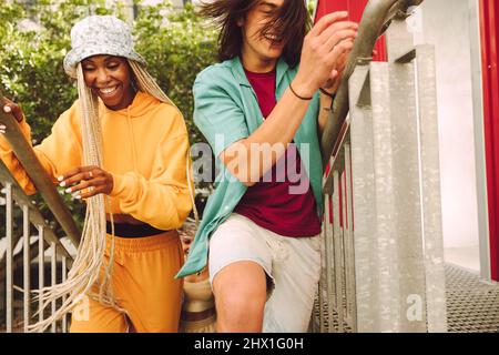 Giovani amici felici che corrono sulle scale all'aperto. Gruppo di giovani allegri sorridenti e che si divertono insieme. Amici multietnici che hanno Foto Stock