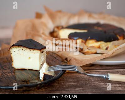 Fetta di cheesecake basca bruciata con un esterno brunito e un interno cremoso custidy su un piatto di vetro marrone. Dessert spagnolo per colazione Foto Stock