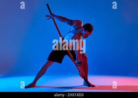 atleta con allenatore bastone karate utilizzando lo strumento sportivo in studio su sfondo di luci colorate. Foto Stock