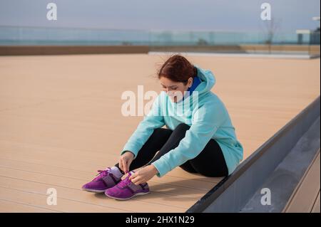 Donna caucasica in una felpa con cappuccio che le legava le scarpe prima di fare jogging. Foto Stock