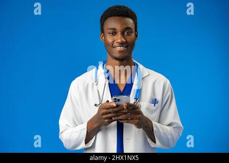 Allegro medico africano utilizzando il telefono cellulare su sfondo blu studio Foto Stock