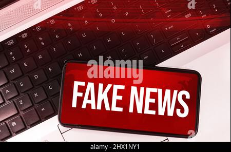 Notizie false sui social media e sui dispositivi mobili con notebook sullo sfondo. Voci e ultime notizie concetto di fondo Foto Stock