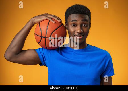 Ritratto di un giovane afroamericano sorridente che tiene un basket su sfondo giallo Foto Stock