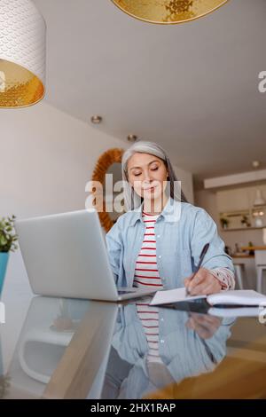 Donna che lavora sul notebook e prende appunti a casa Foto Stock