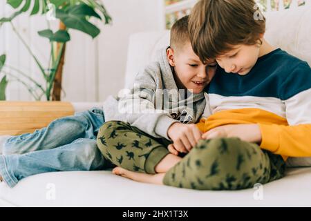 Allegro due ragazzi bambini che giocano online, guardando video sul cellulare. Sorridendo i bambini con divertenti app mobili, godendo del tempo libero a casa Foto Stock