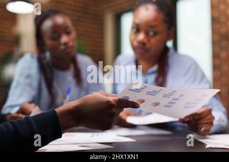 Focalizzazione selettiva della mano del dipendente che ha un grafico di gestione durante l'incontro con i colleghi. Colleghi aziendali che esaminano i piani finanziari aziendali e la documentazione contabile. Foto Stock