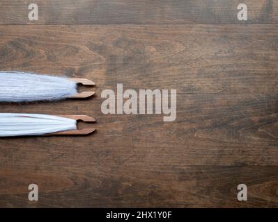 Sfondo di legno marrone con due navette tessenti piene di filo rosa chiaro, spazio copia. Concetto di artigianato, tessitura, lavorazione tessile Foto Stock