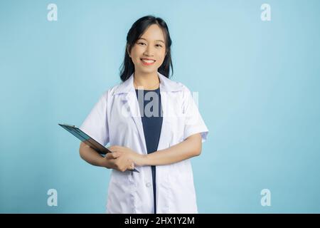 Ritratto di giovane asiatico bella infermiere in uniforme bianca con grande sorriso tenendo appunti del foglio di controllo paziente su sfondo blu spazio copia Foto Stock