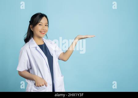 Ritratto di giovane asiatico bella infermiera in uniforme bianca con grande mano sorridente mostra per presentare il tuo prodotto o testo su spazio copia sfondo blu Foto Stock