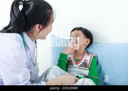 Bambino felice che ha malattia respiratoria aiutato dal professionista della salute con inalatore. Pediatra prendersi cura del ragazzo asiatico con problemi di asma rendendo l'inalazione Foto Stock