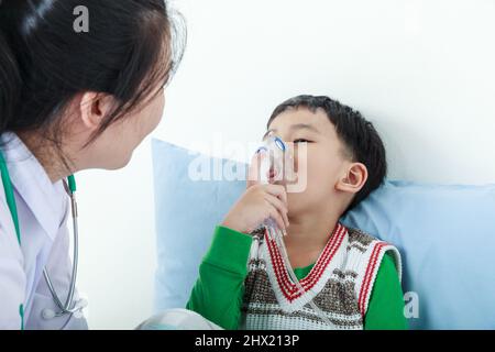 Triste bambino che ha malattia respiratoria aiutato da professionista di salute con inalatore. Pediatra prendersi cura ragazzo asiatico con problemi di asma rendendo inalati Foto Stock