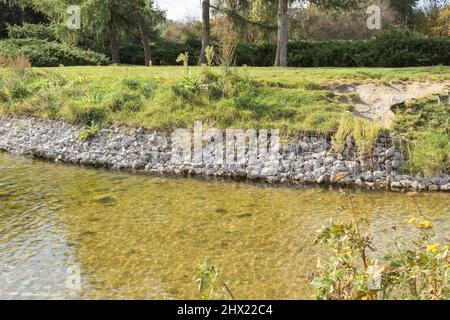 Rafforzare le rive del fiume, rete e pietre. Paesaggio riva del fiume e grandi pietre con rete metallica Foto Stock