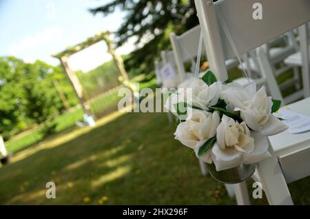 Sedie bianche adornate con tessuti bianchi Rose Bouquets attendono gli ospiti ad un matrimonio Giardino Foto Stock