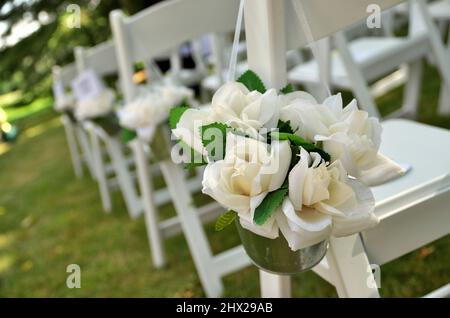 Sedie bianche adornate con tessuti bianchi Rose Bouquets attendono gli ospiti ad un matrimonio Giardino Foto Stock